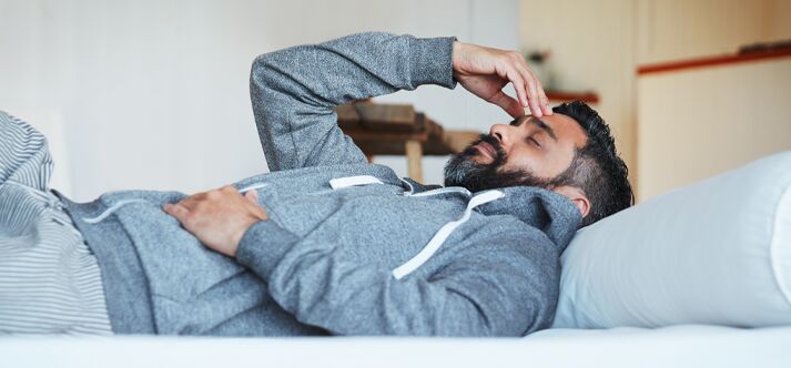 Homem deitado na cama parecendo pensativo.