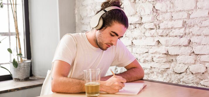Jovem escrevendo com fones de ouvido em ambiente descontraído.